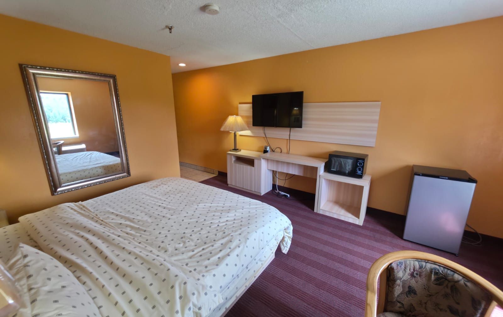 A hotel room with a bed, a desk, a television, and a refrigerator.