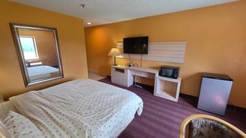 A hotel room with a bed, a desk, a television, and a refrigerator.