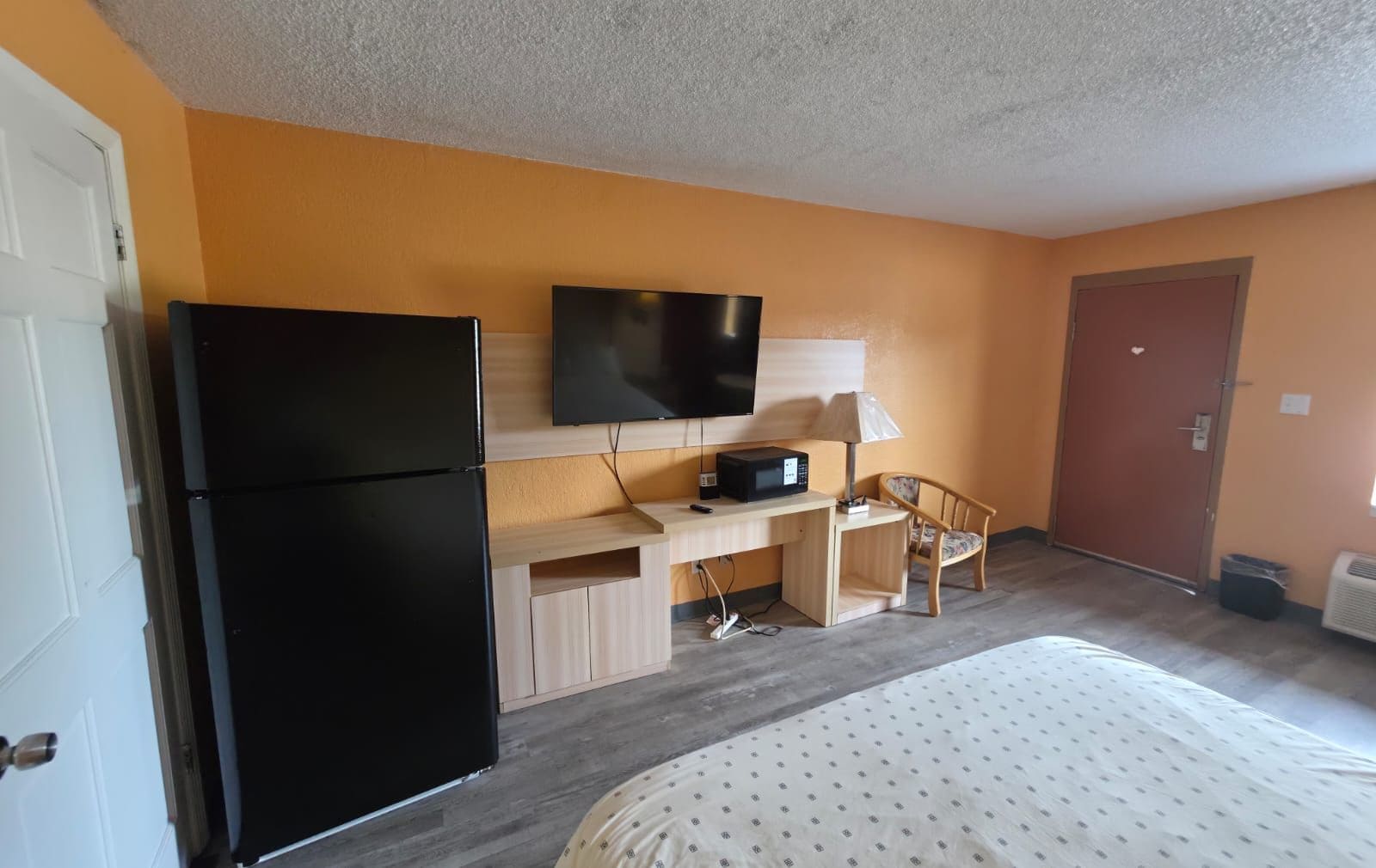 A hotel room with a bed, a desk with a television, a refrigerator, and a chair.