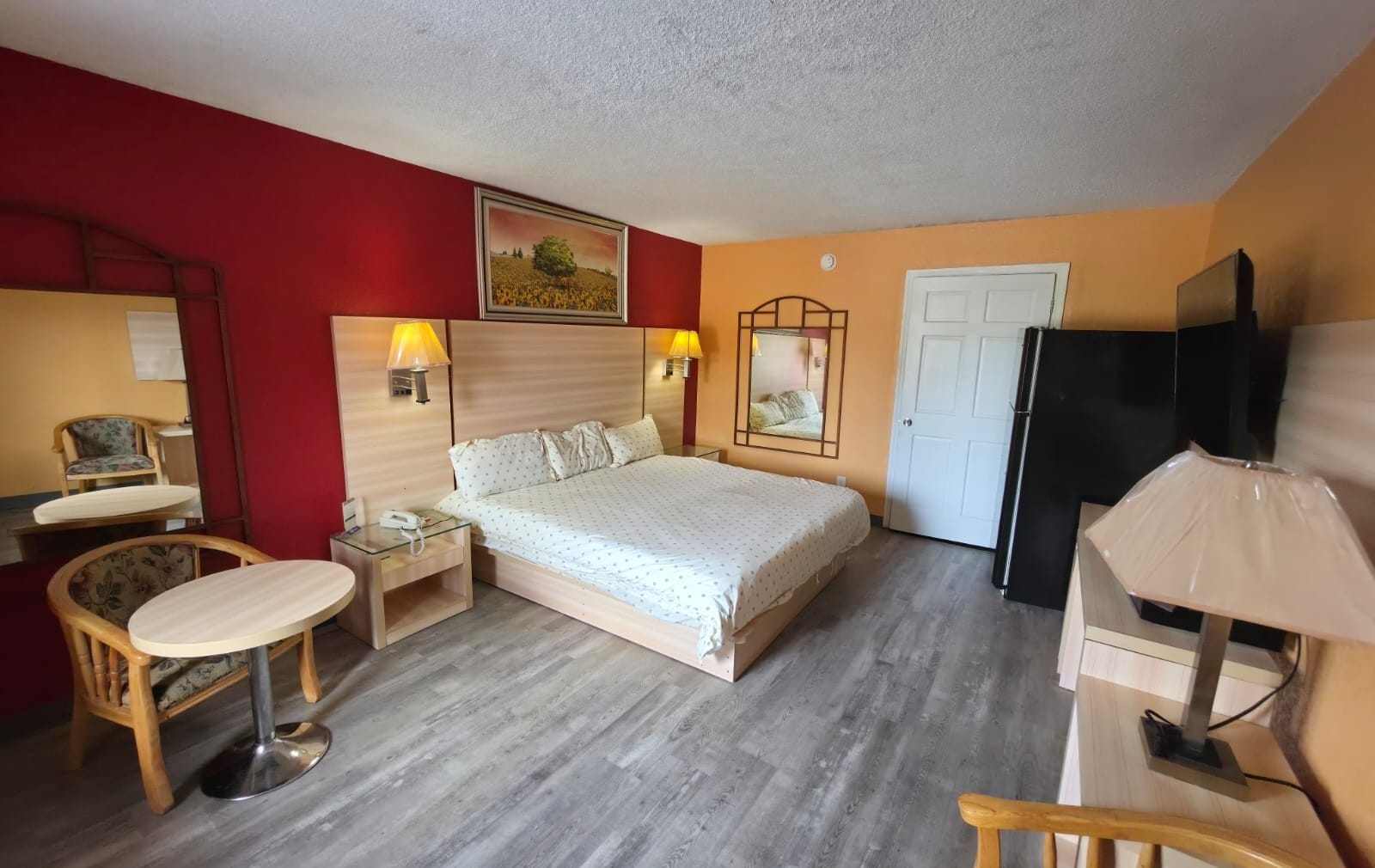 A hotel room with a bed, bedside tables, a chair, a desk, a television, and a door.