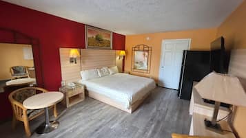 A hotel room with a bed, bedside tables, a chair, a desk, a television, and a door.