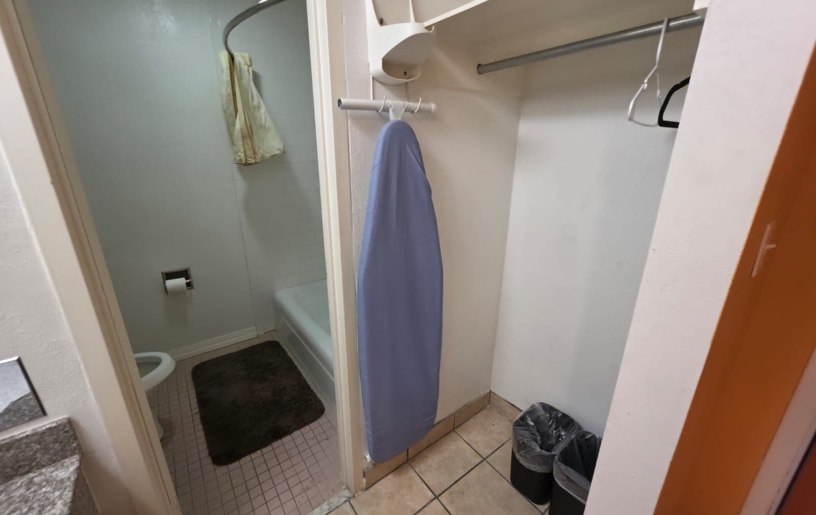 A small bathroom with a toilet, a shower, a towel rack, and two trash bins.