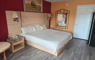 Un dormitorio con cama, mesitas de noche, un espejo, una puerta y un teléfono de pared.
