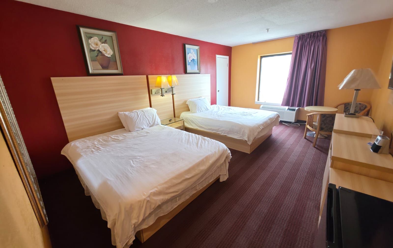 A hotel room with two beds, a desk, a chair, and a window with curtains.