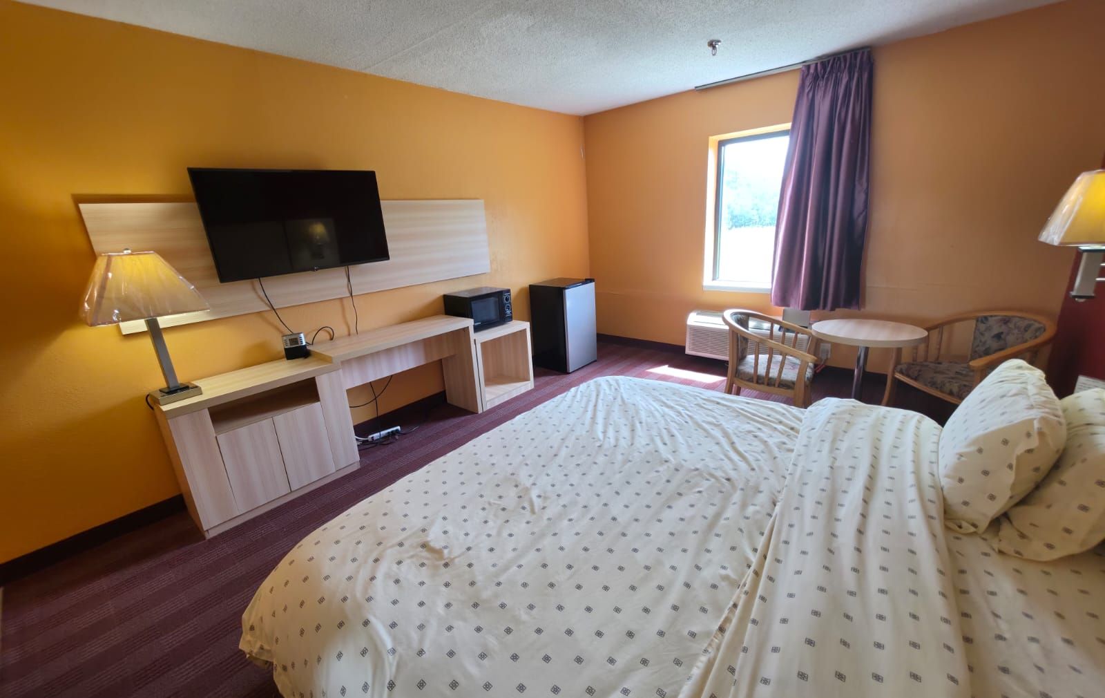 Una camera d'albergo con un letto, una scrivania con TV a schermo piatto, una sedia, un tavolino e una finestra con tende.