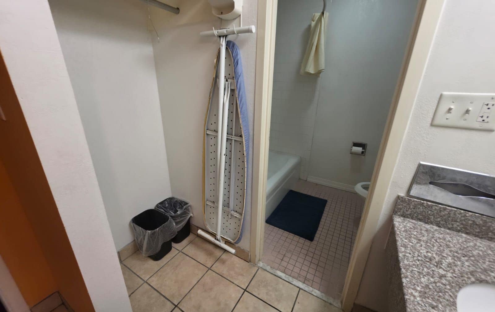 A bathroom with a shower, a toilet, a trash bin, and a towel rack.