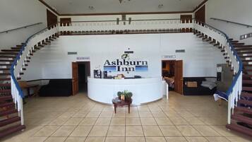 A hotel lobby with a reception desk, a staircase, and signs for restrooms and the office.