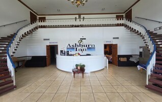 Un hall de hotel con mostrador de recepción, una escalera y señalización para los baños y la oficina.