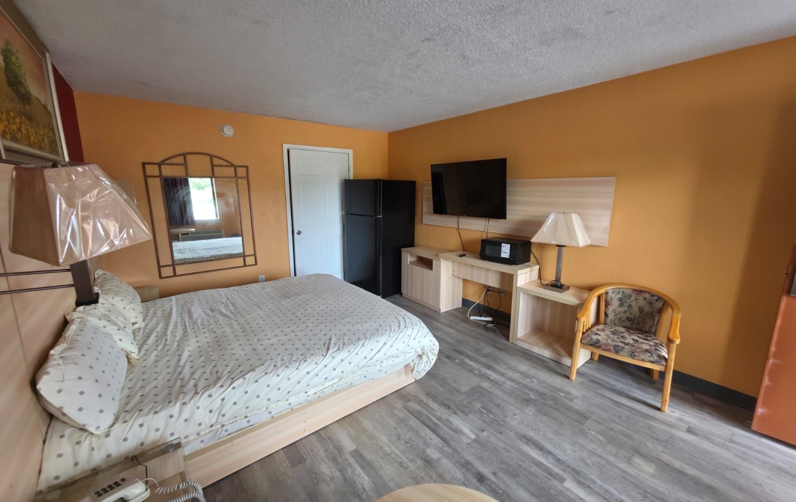 A hotel room with a bed, a desk, a chair, a television, and a door.