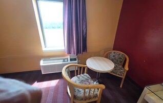 Habitación de hotel con una cama, una mesa redonda, dos sillas, una ventana con cortinas y un equipo de aire acondicionado.