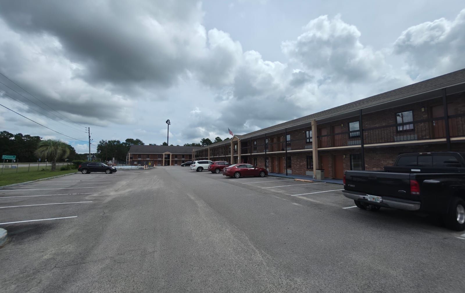 A multi-story motel with a parking lot, several cars parked, and a cloudy sky.