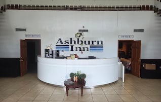 Mostrador de recepción en Ashburn Inn con indicaciones para baños y oficina, una pequeña mesa con una planta y un suelo de baldosas.