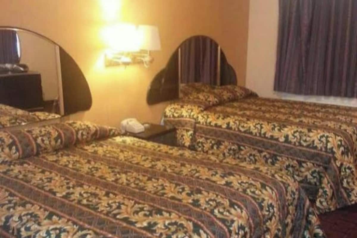 Quarto de hotel com duas camas, mesa de cabeceira, abajur e janela com cortinas.