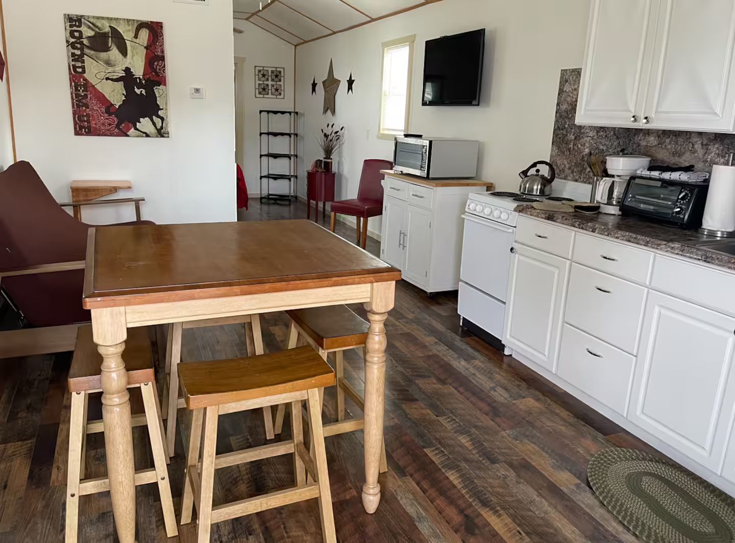 Una cocina compacta con una mesa de madera, armarios blancos y un microondas.
