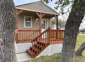 A two-story wooden cabin with a porch and a small window.