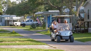 A residential street with houses, a parked truck, and a golf cart with two passengers.