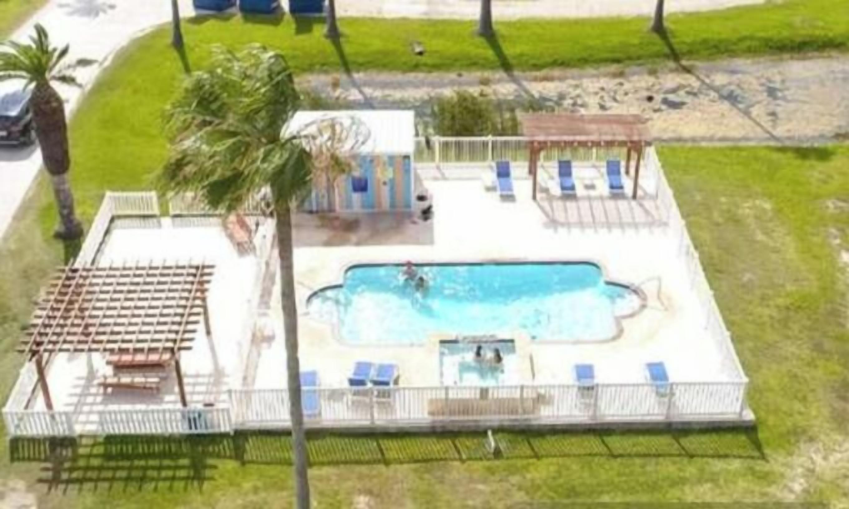 Una piscina con sillas de descanso y un toldo, rodeada de un área cercada y un césped.