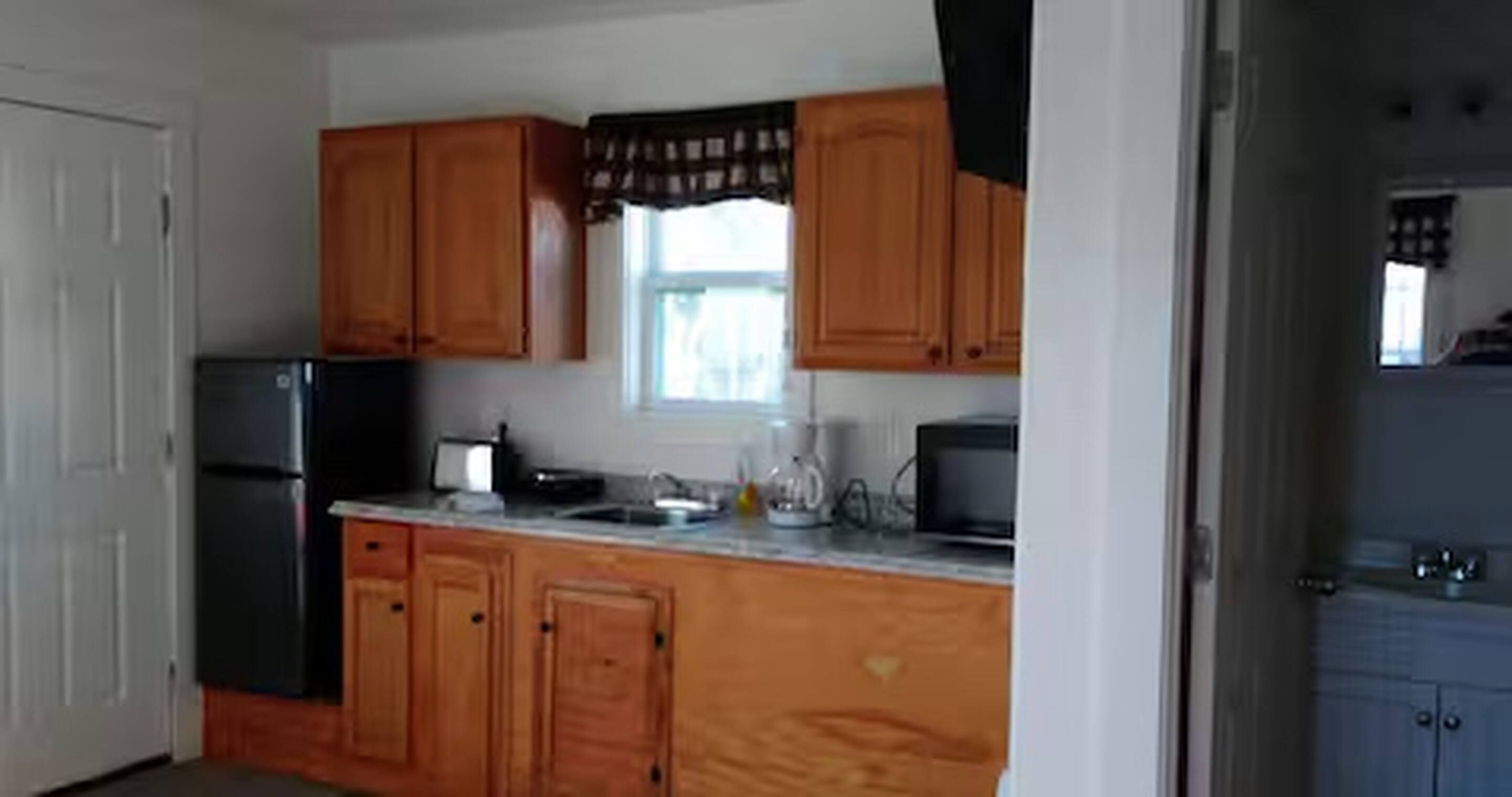 Una cocina con armarios de madera, un refrigerador, un microondas y una ventana con cortinas.