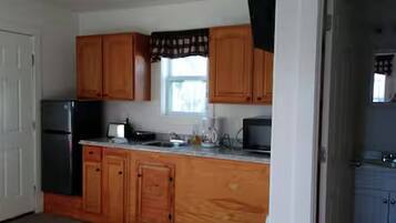 Una cocina con armarios de madera, un refrigerador, un microondas y una ventana con cortinas.