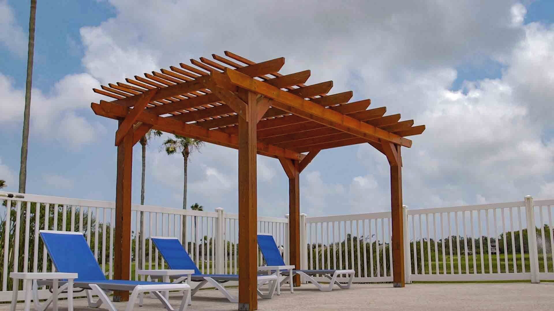 Une structure de pergola en bois, agrémentée d’une clôture blanche et de chaises longues bleues.