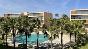 A modern hotel with a pool surrounded by palm trees and a clear blue sky. - Herdade dos Salgados, 3-Bedroom Apartment 8E-1C, Vila das Lagoas (Albufeira)