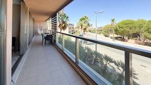 A balcony with a table and chairs, overlooking a street with palm trees and buildings. - Herdade dos Salgados, 3-Bedroom Apartment 8E-1C, Vila das Lagoas (Albufeira)