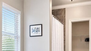Un baño con inodoro, cortina de ducha, un cuadro en la pared y una alfombra blanca en el suelo.