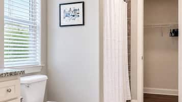 Ein Badezimmer mit Toilette, einer Duschkabine, einem gerahmten Bild an der Wand und einem weißen Teppich auf dem Boden.