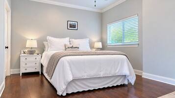 A bedroom with a bed, nightstands, a ceiling fan, a window with blinds, and a door.