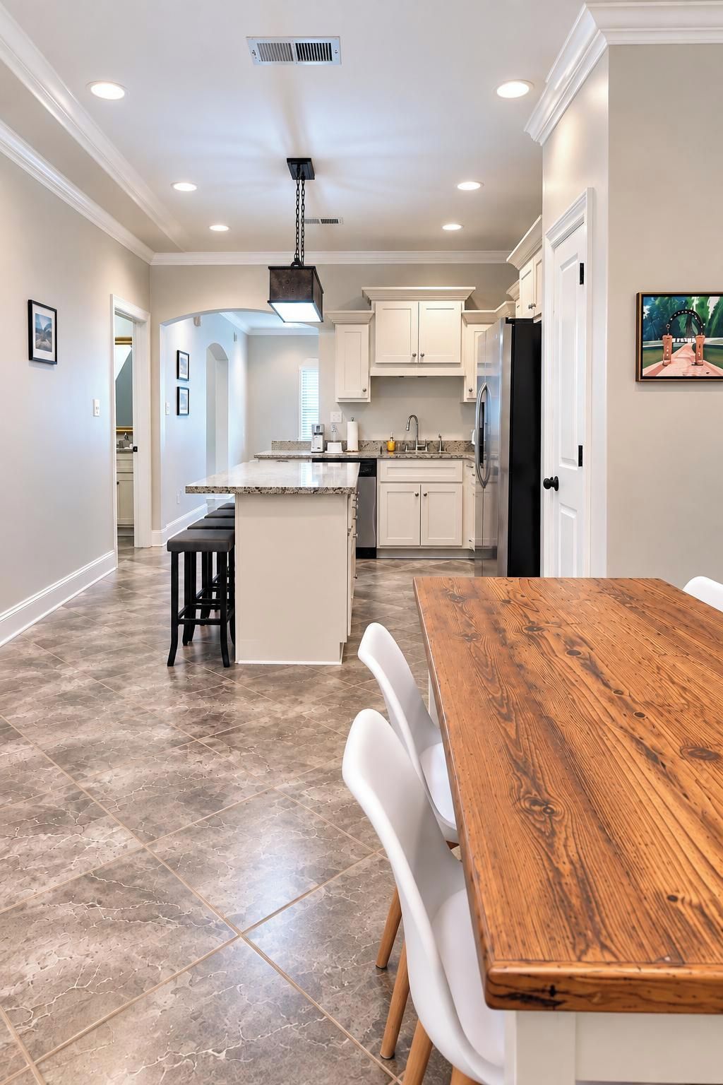 Una cocina amplia con una isla central, muebles blancos y un comedor con mesa de madera y sillas blancas.