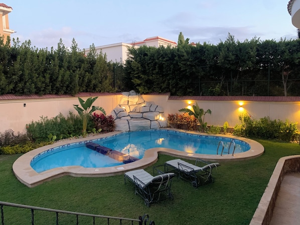 A swimming pool with a unique shape, surrounded by a well-maintained lawn and various plants.