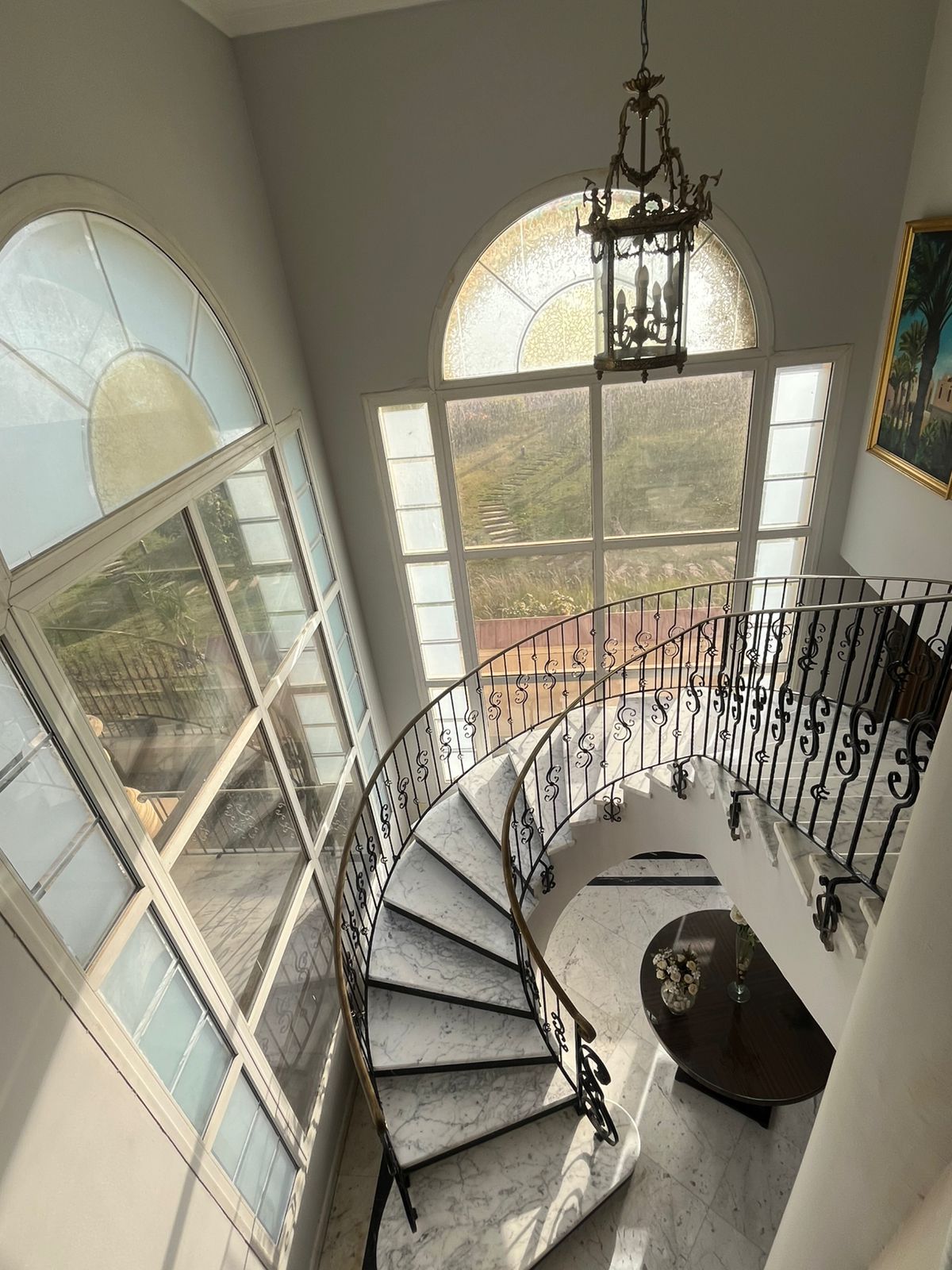 Un escalier en colimaçon avec des finitions en marbre, de grandes fenêtres en arc de cercle et un lustre.