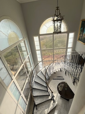 A spiral staircase with a marble finish, large arched windows, and a chandelier.