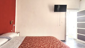 A hotel room with a bed, a television mounted on the wall, and a door leading to a balcony. - Garden, Terrace and Private Parking (Orgosolo)