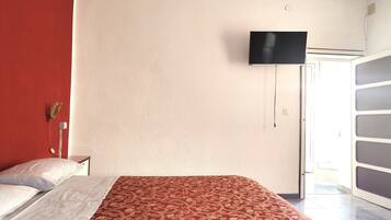 A hotel room with a bed, a television mounted on the wall, and a door leading to a balcony.