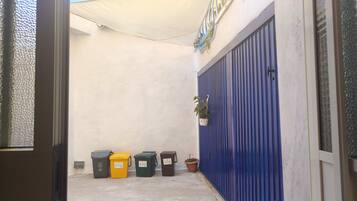 A narrow alleyway with a blue metal gate, a white wall, and a yellow tarp overhead.