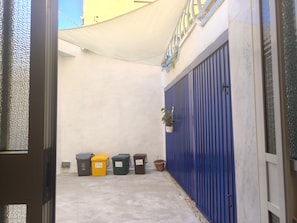 Un estrecho callejón con una reja de metal azul, una pared blanca y un toldo amarillo.