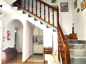 Una escalera con balaustres de madera, una pared blanca con cuadros enmarcados y una zona de cocina con armarios y un lavabo.