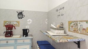 A kitchen with a coffee maker, a kettle, and a shelf with kitchen items. - Garden, Terrace and Private Parking (Orgosolo)