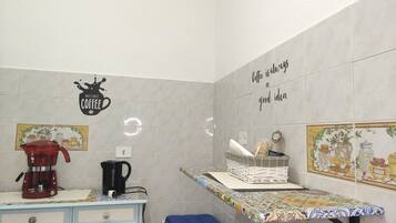 A kitchen with a coffee maker, a kettle, and a shelf with kitchen items.