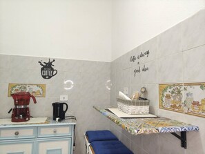 Una cocina con cafetera, hervidor y una estantería con utensilios de cocina.
