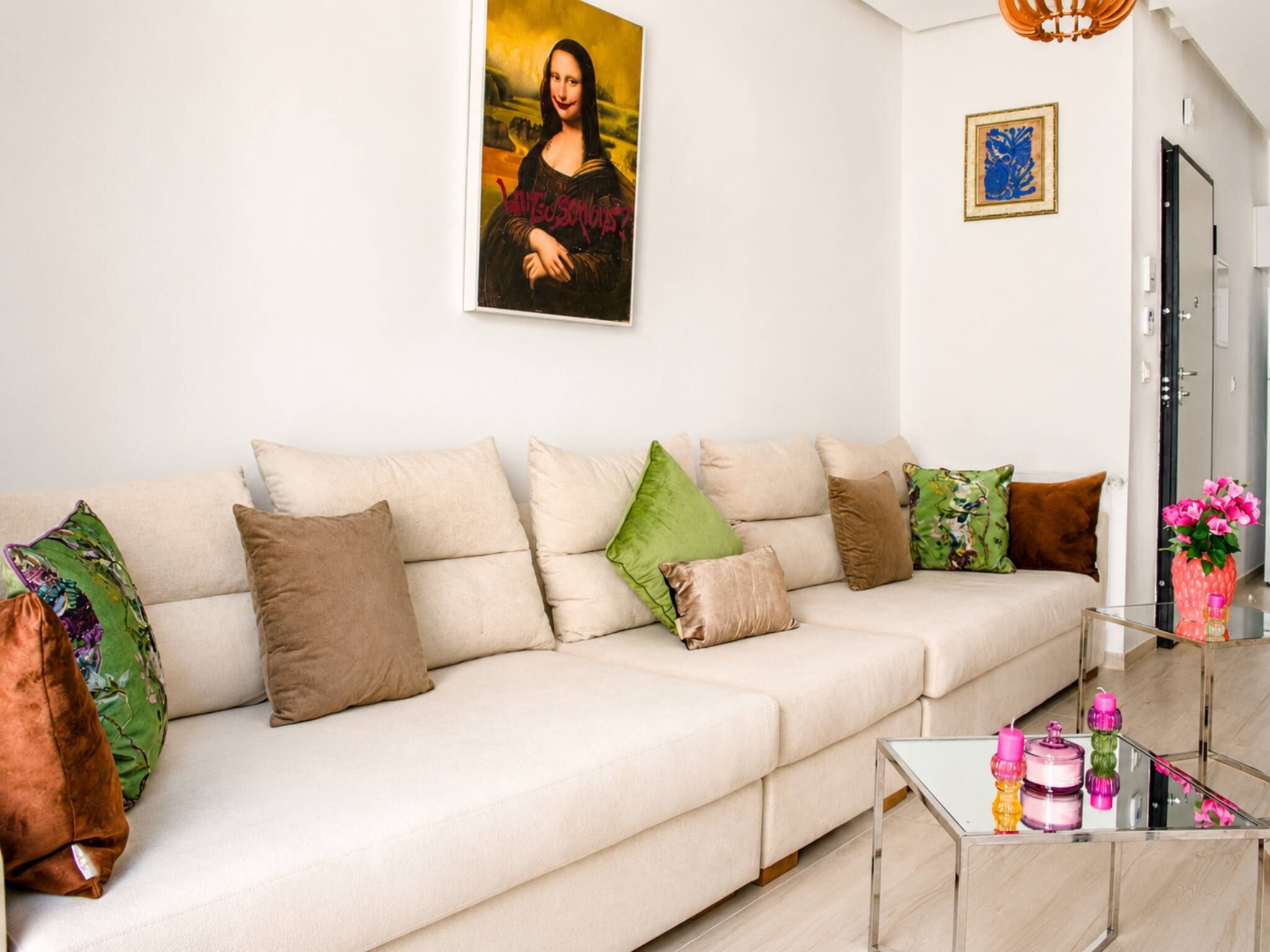 Una sala de estar moderna con un sofá, cojines, una mesa de centro de vidrio y un cuadro en la pared.