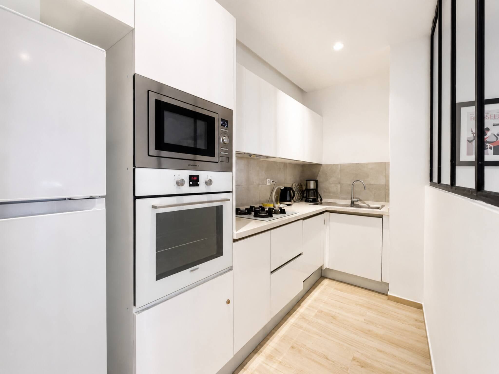A modern kitchen with white cabinetry, stainless steel appliances, and a wooden floor.