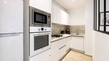 A modern kitchen with white cabinetry, stainless steel appliances, and a wooden floor.