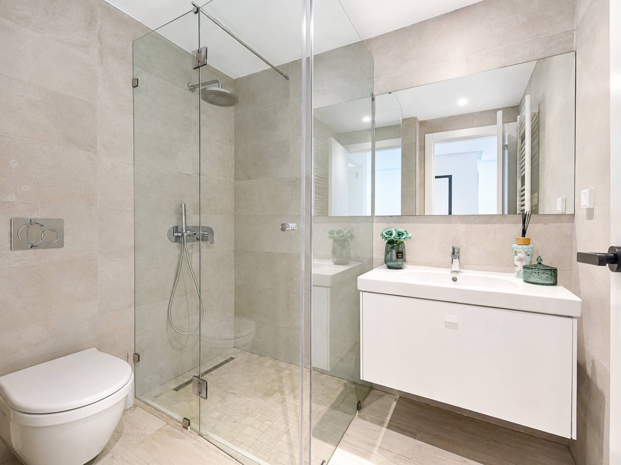 A modern bathroom with a glass-enclosed shower, a white toilet, and a vanity with a mirror.
