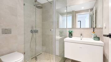 A modern bathroom with a glass-enclosed shower, a white toilet, and a vanity with a mirror.