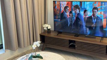 A living room with a flat-screen TV on a wooden stand, a round marble coffee table with a remote control, a box of tissues, and a potted orchid.
