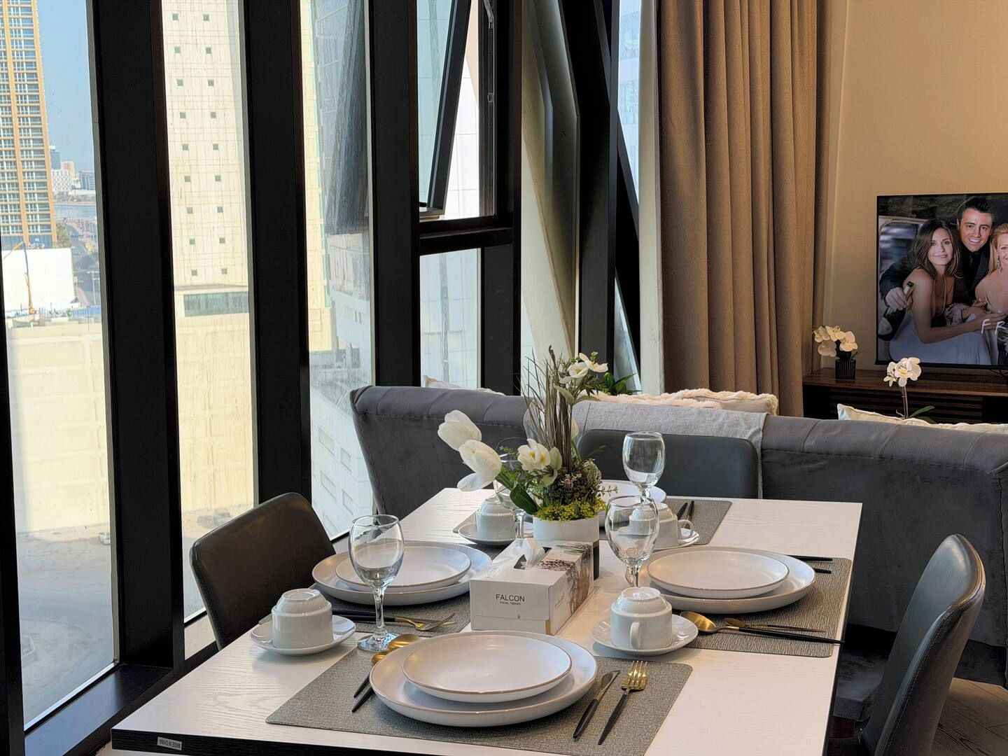 A dining area with a table set for two, a sofa, and a television.
