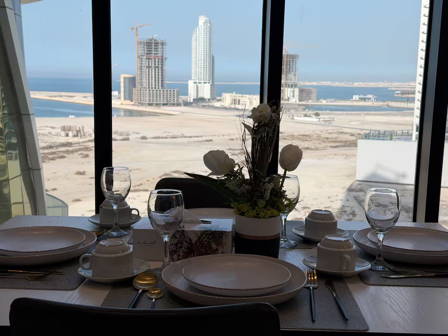 A dining table set for two with a view of a beach and cityscape.