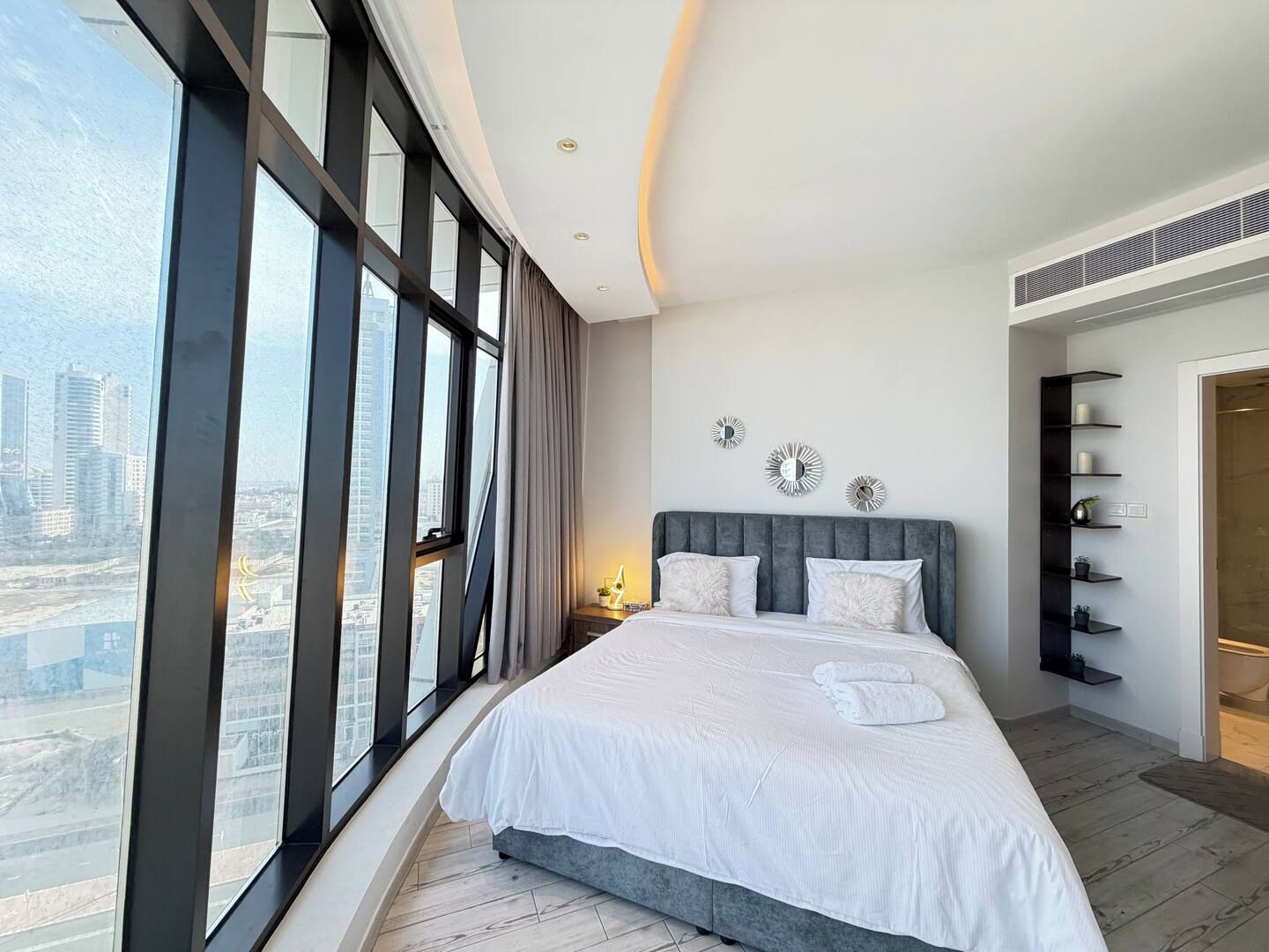 A modern bedroom with a large bed, city view, and built-in shelving.